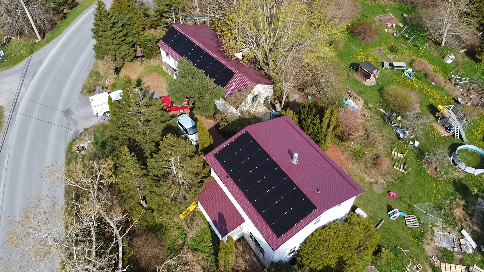 Two red-roofed buildings with solar panels, surrounded by trees